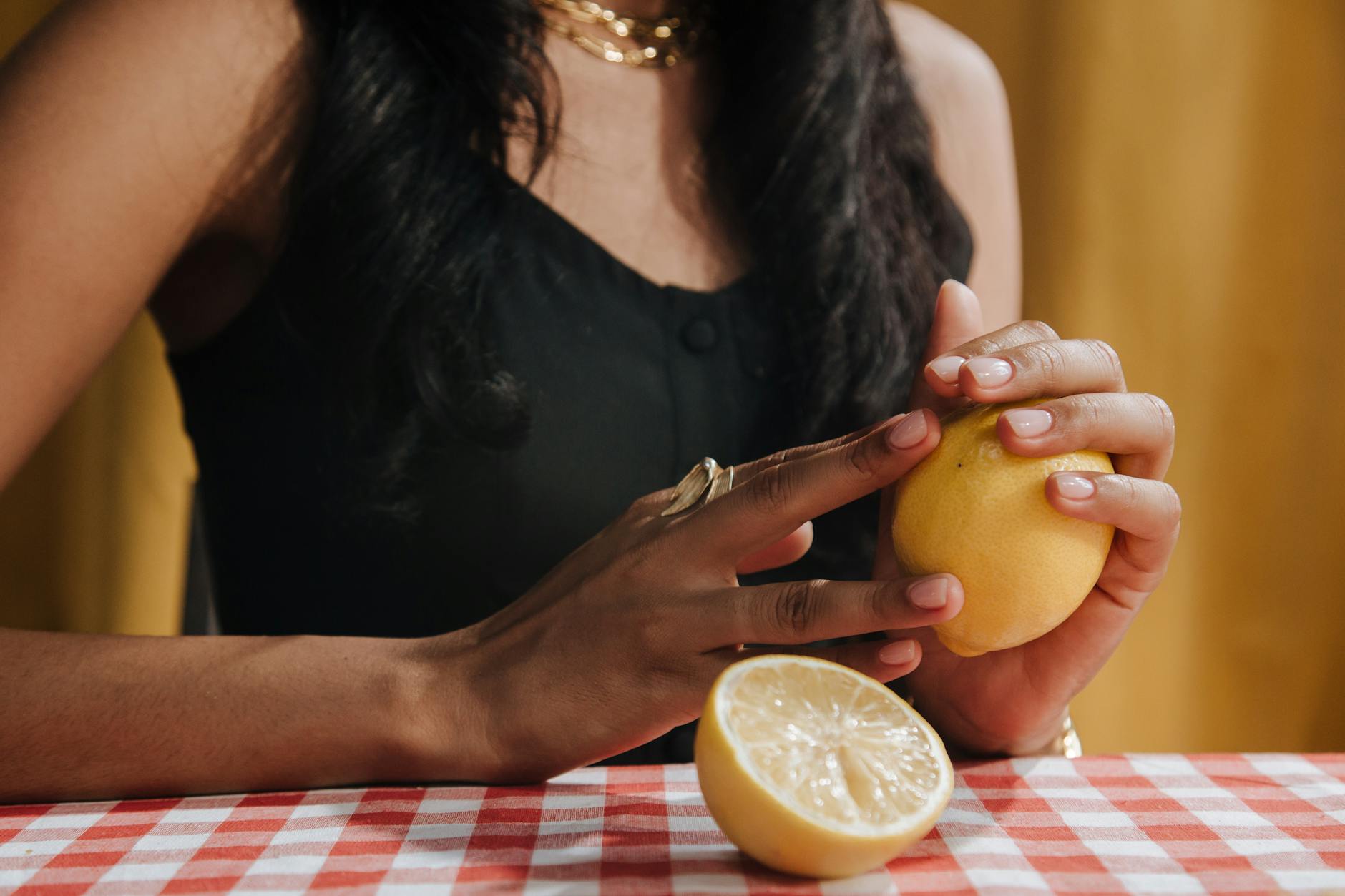 Hand holding a fresh lemon on a soft pink background with additional lemons, representing natural cycles and wellness