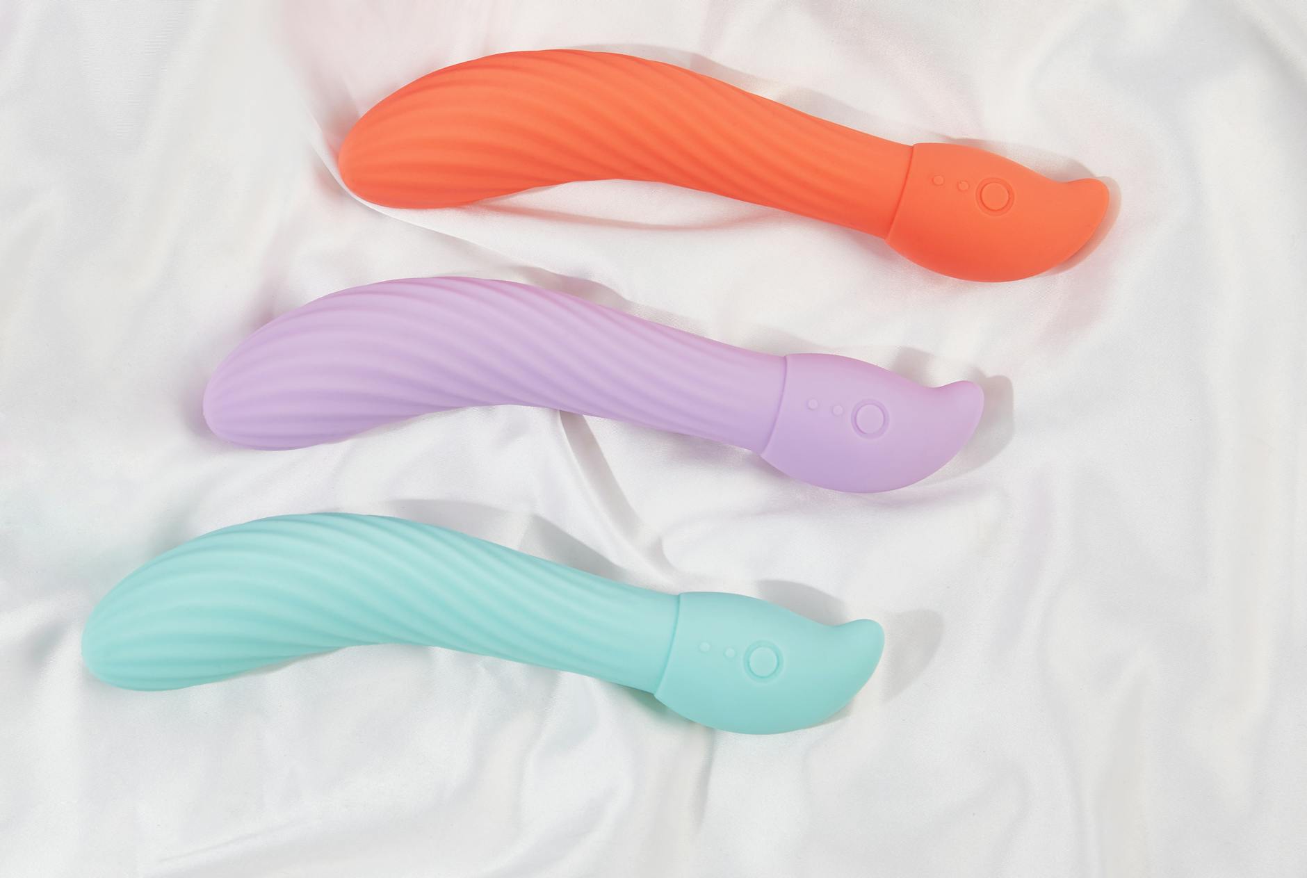 Colorful vibrators arranged on white fabric, representing diverse sexual wellness options post-surgery