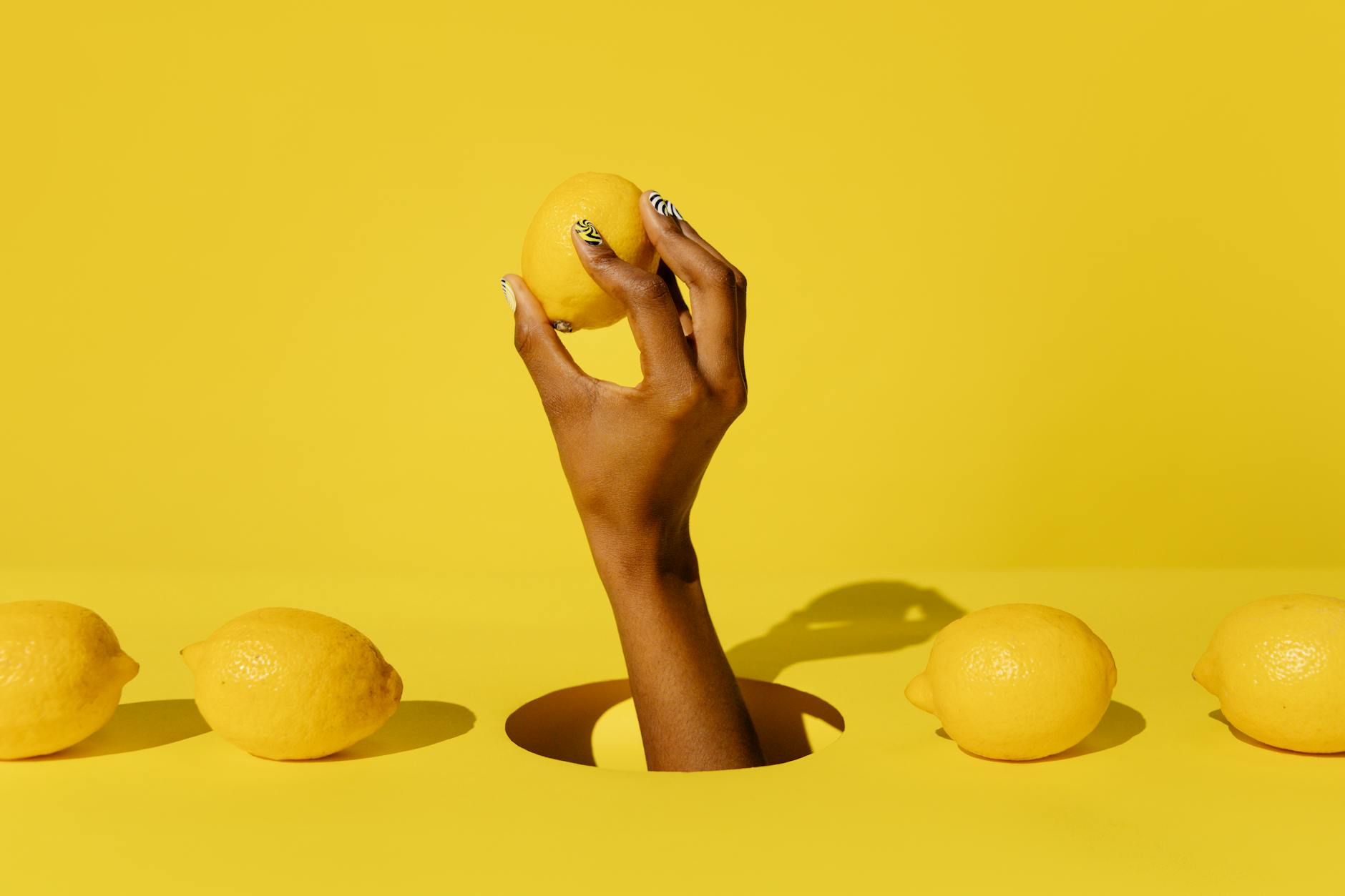 A hand holding a fresh lemon against a bright yellow background, symbolizing the fresh start of exploring lemon vibrators