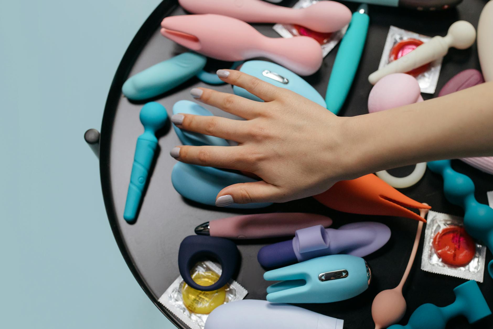 A hand reaching over a variety of colorful clitoral vibrators arranged on a table