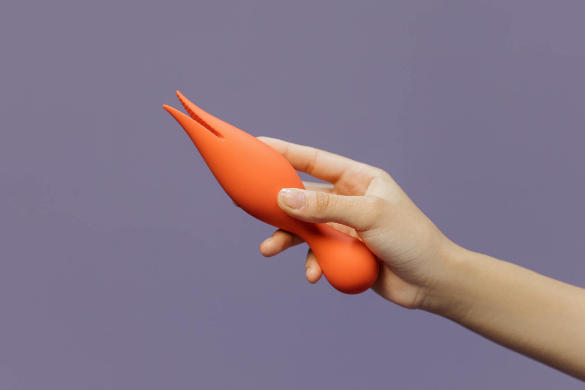 Close-up of a hand holding a lemon-colored vibrator against a minimalistic purple backdrop