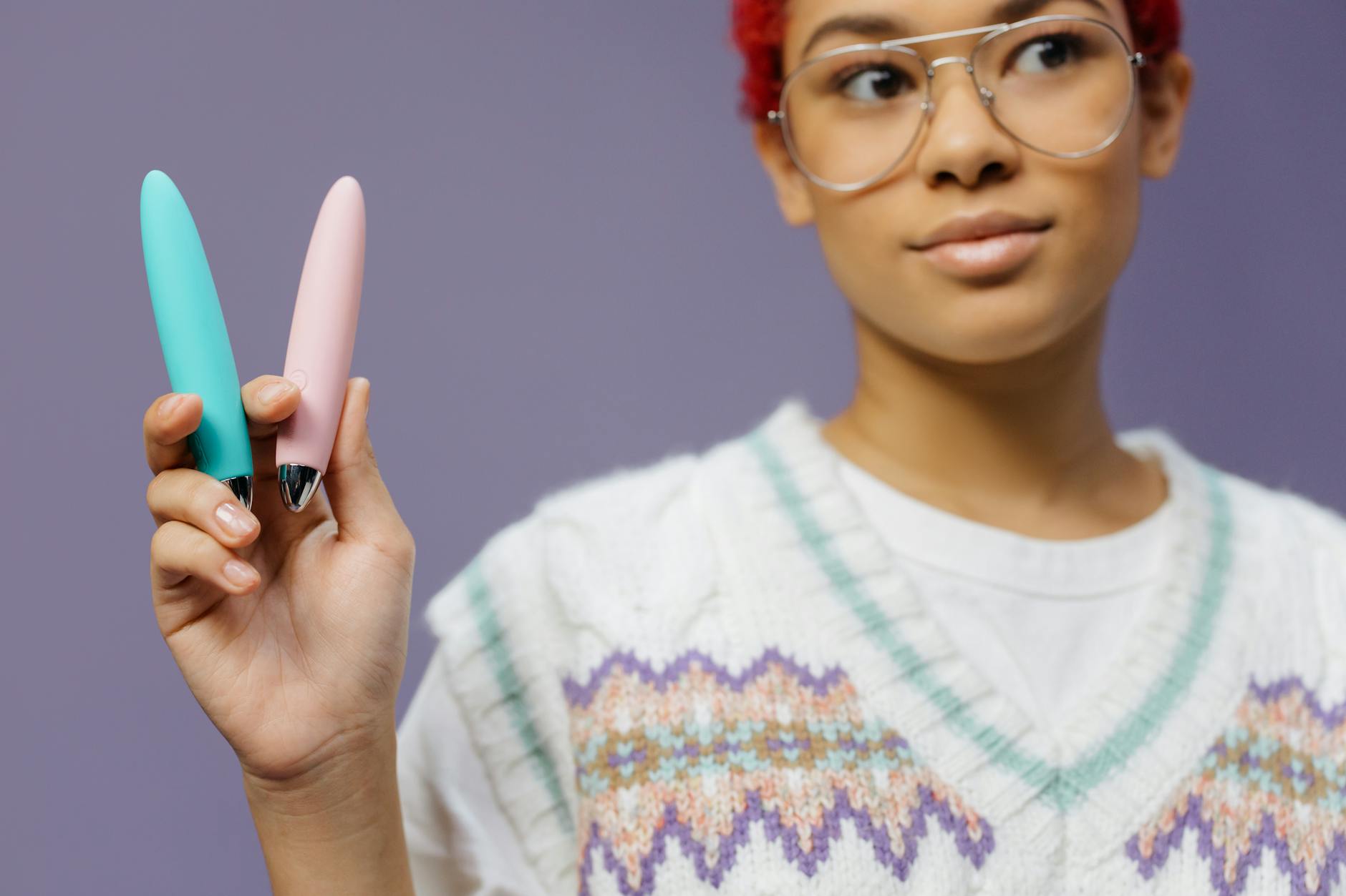 Woman holding colorful vibrators and clitoral stimulation devices against a purple background