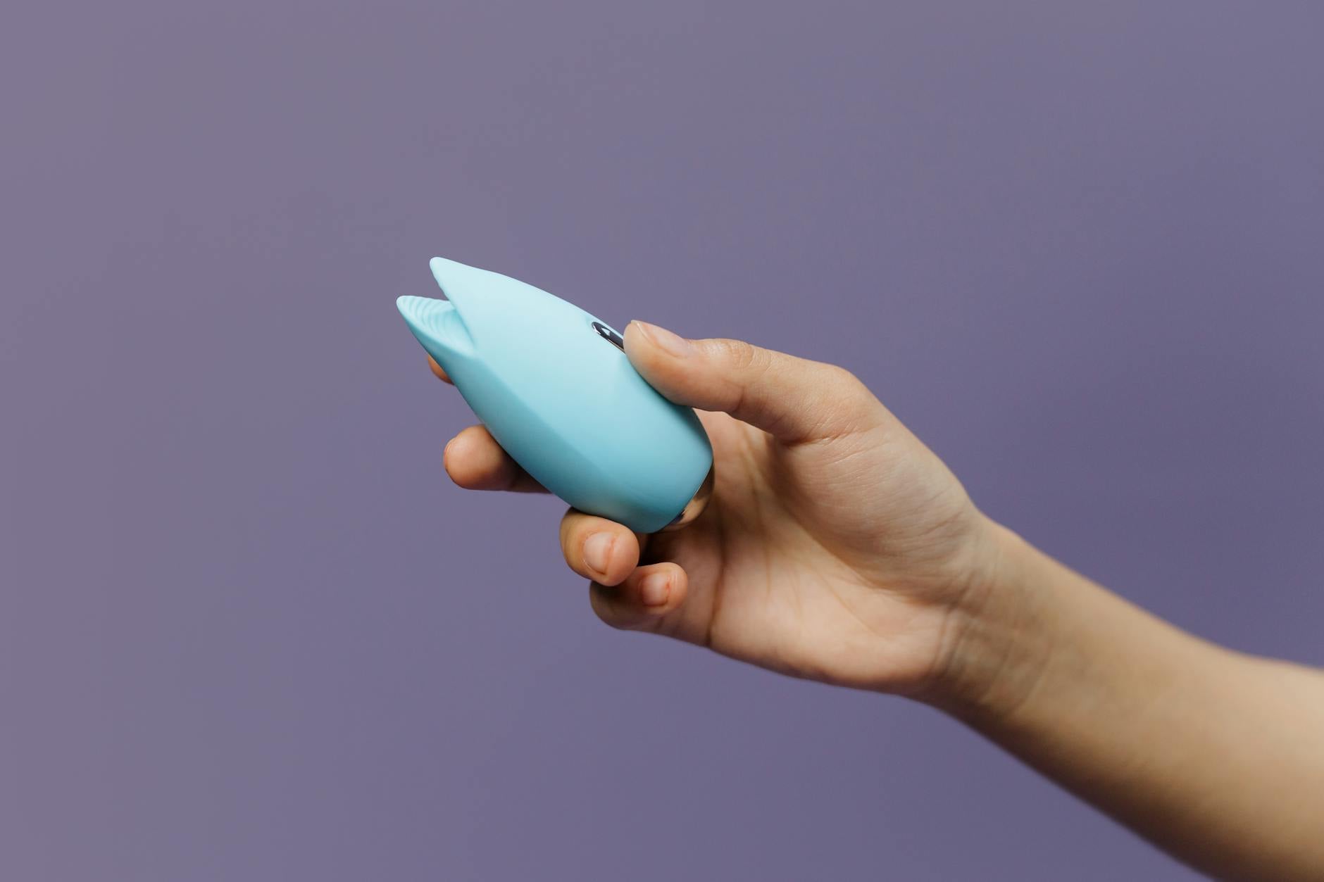 A blue silicone sex toy held in hand against a solid purple background, promoting self-love and sexuality