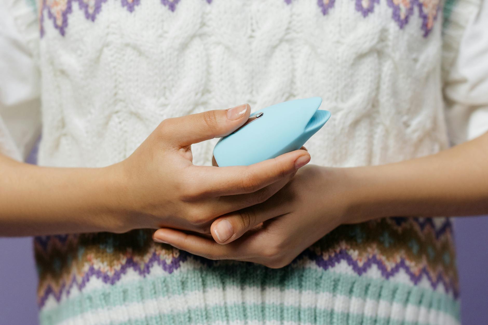 Close-up of hands holding a blue personal vibrator against a knitted sweater during recovery.