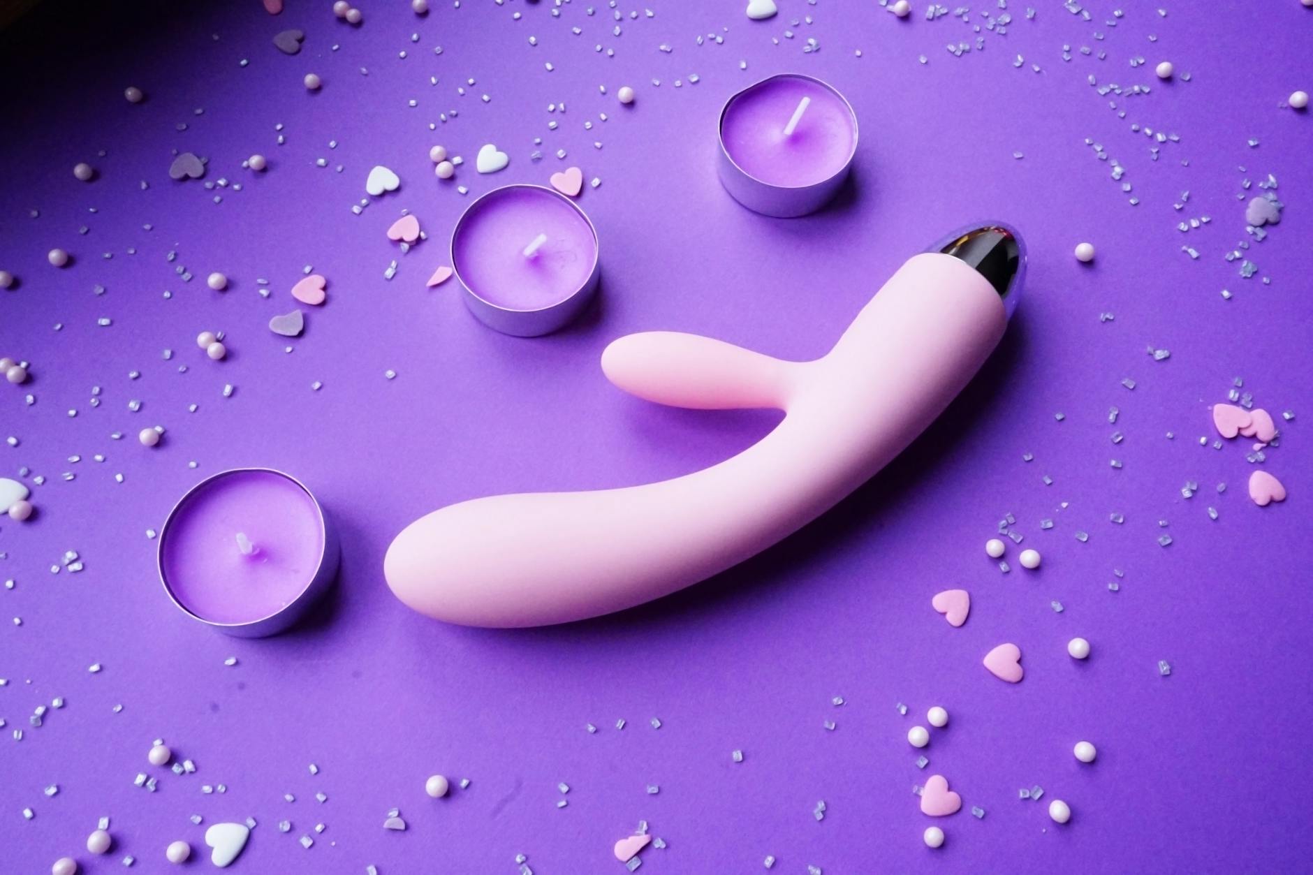 Vibrant pink vibrator on purple background with heart confetti and candles for intimate moments